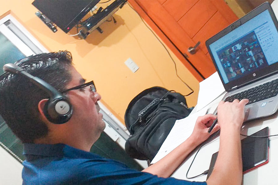 El Dr. Rolando dando clases en línea, con audífonos y escribiendo en una laptop