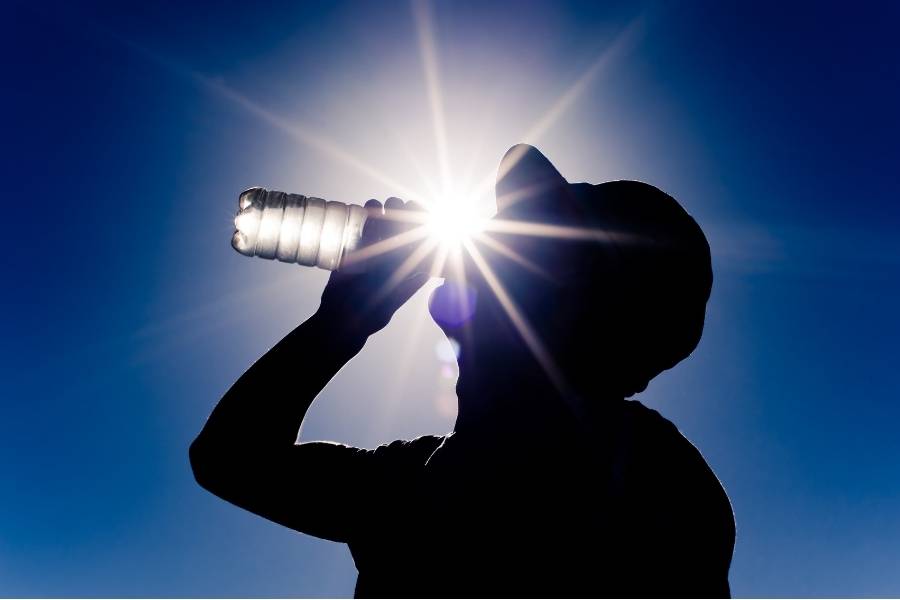 Persona tomando agua de una botella frente a altas temperaturas.