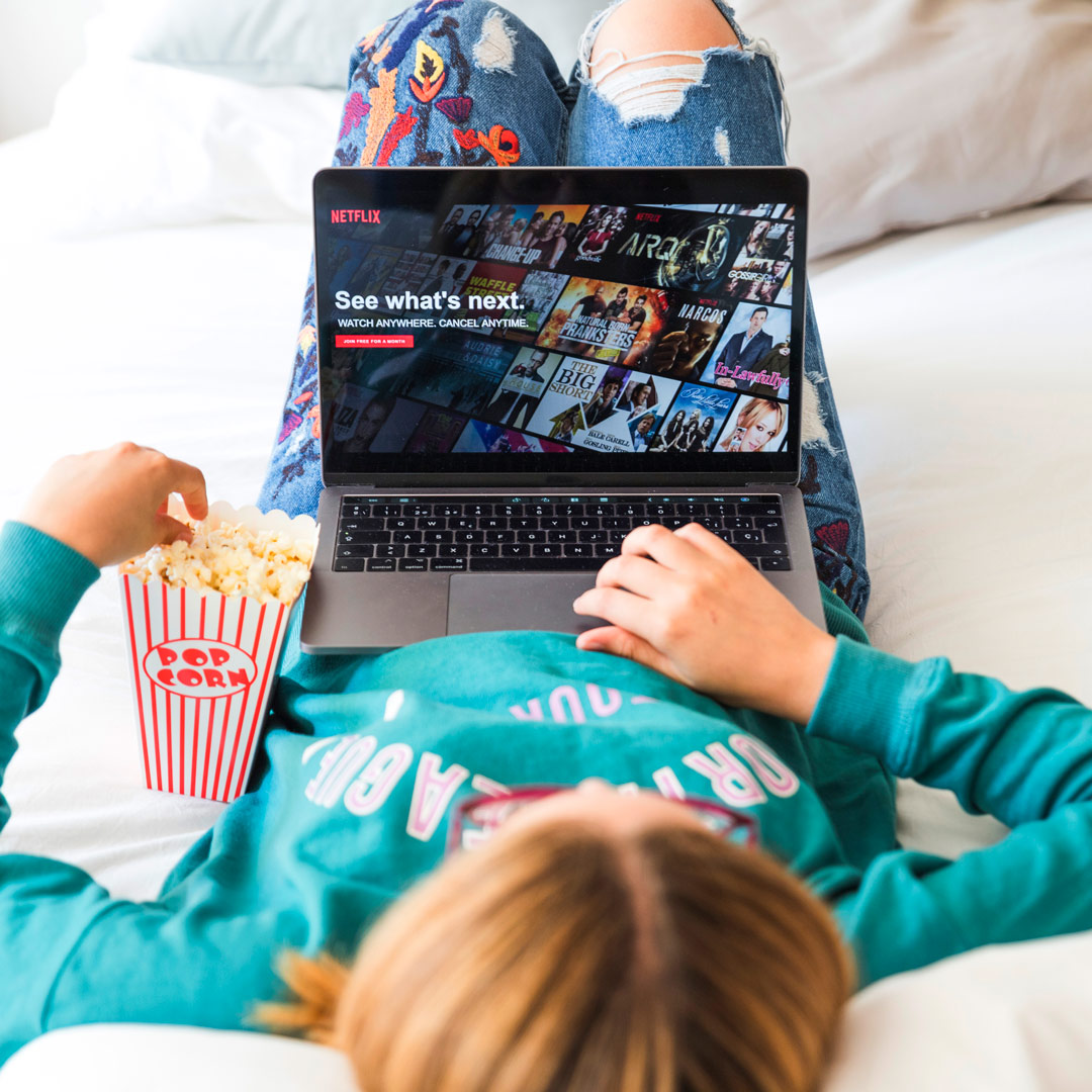 Mujer acostada con laptop viendo Netflix