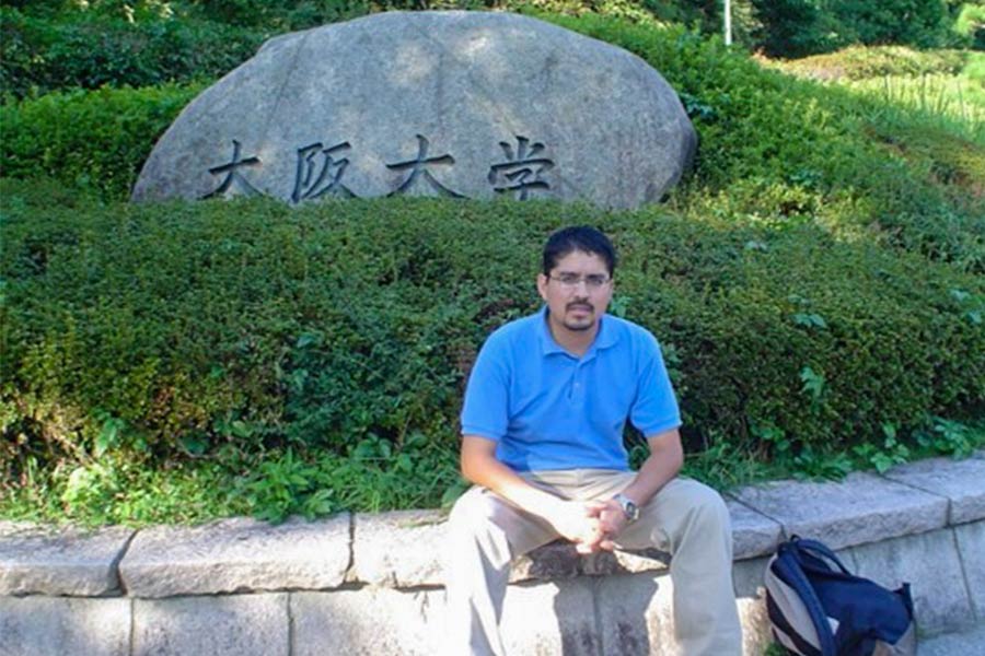 Dr. Rolando sentado, mirando a la cámara en un jardín, detrás una roca con signos japoneses