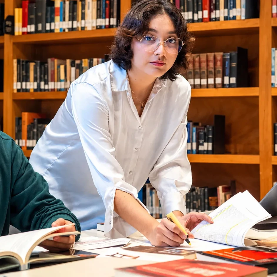Estudiantes y profesora colaborando en la biblioteca y revisando libros.