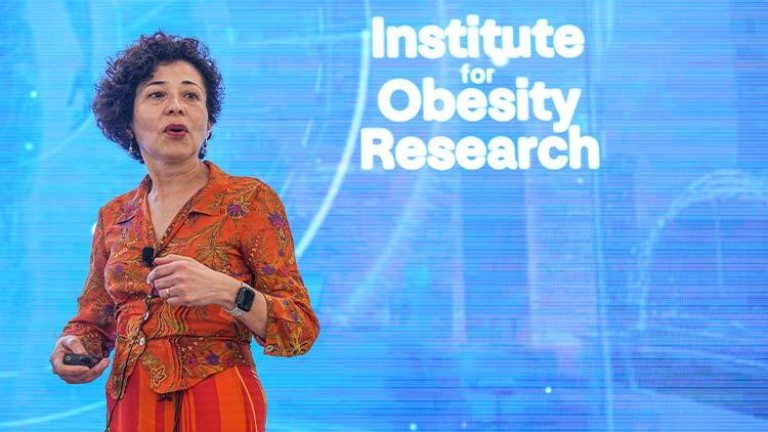 imagen de Rosa María Guéant, experta en bioquímica metabólica con un vestido naranja hablando en una conferencia