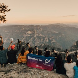 Jovenes sostienendo cámaras fotográficas sentados en un acantilado