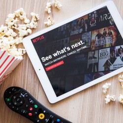 Ipad con Netflix en pantalla a un lado de palomitas y control remoto 