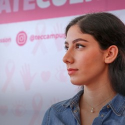 Joven mexicana, detrás de ella se encuentra un anuncio para motivar a prevenir el cáncer de mama